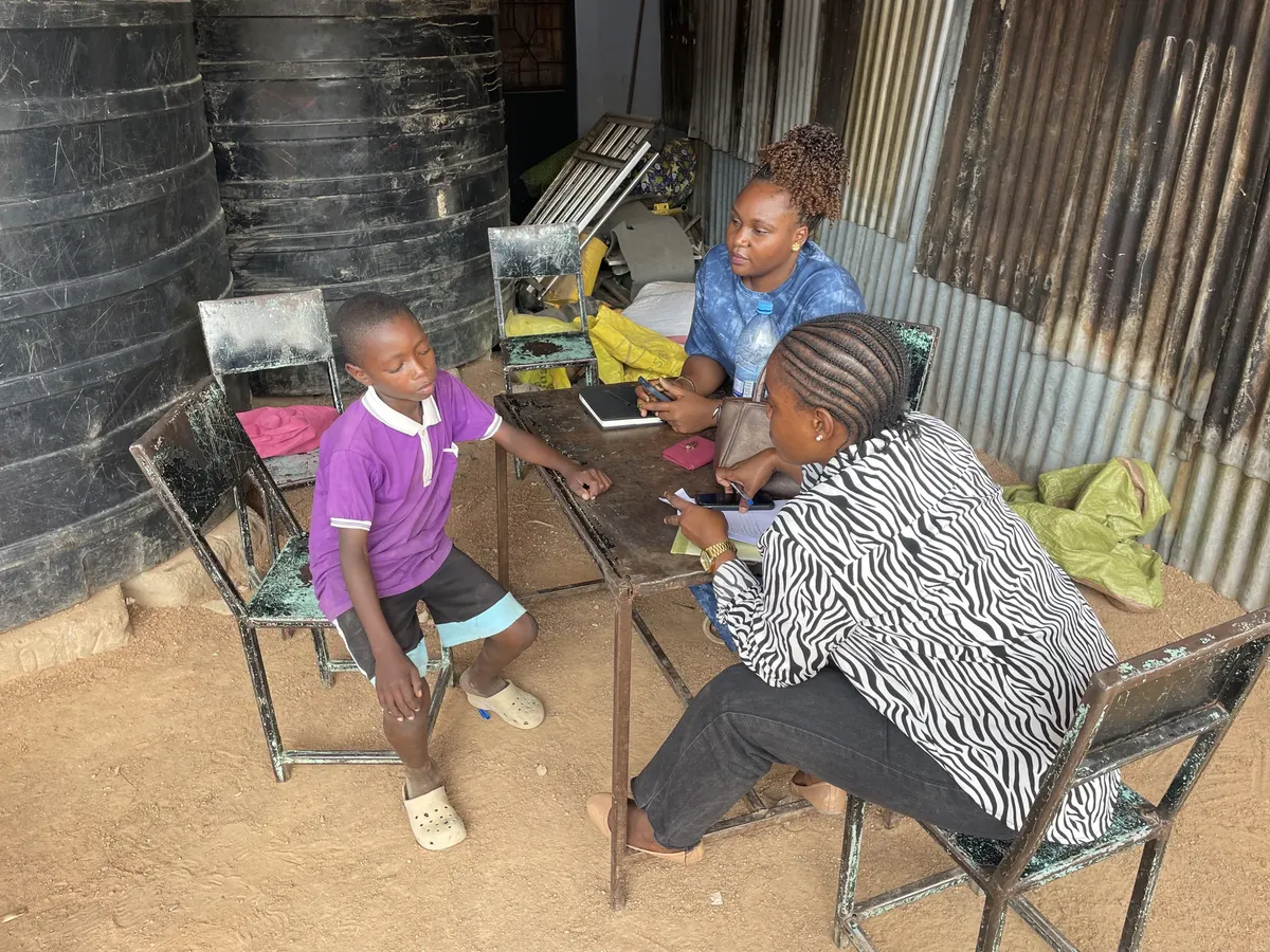 Two government social workers sitting with a child at Watoto Wa Africa during a routine visit